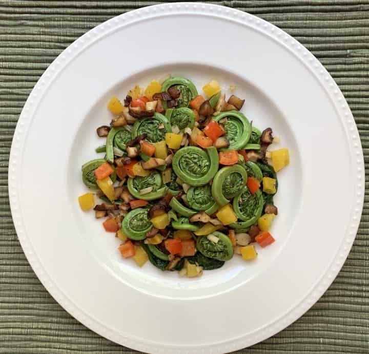 Fiddleheads & Ramps Sauté on a white plate over a sage green placemat