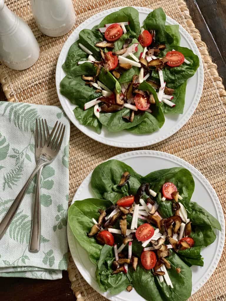 Spinach salad plated with roasted shitiake mushrooms, tomatoes, sliced radiahes & turnips
