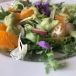 Frisée & Citrus Salad on a plate topped with avocado dressing and edible flowers