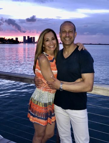 Chef Cindy pictured with her husband Rich and a colorful sky in Miami, waterside
