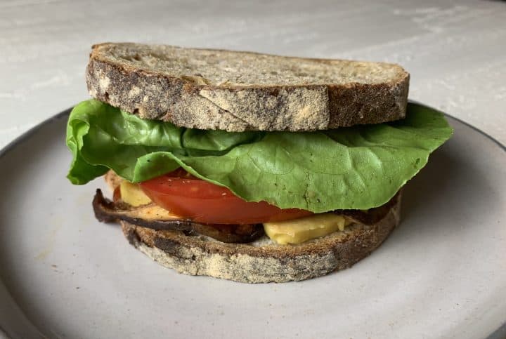 A sandwich on a plate, made with roasted shiitake mushrooms, lettuce, tomato, and vegan cheese 