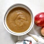 Applesauce in bowl with 2 whole apples alongside