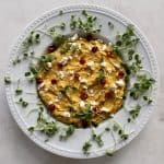 Butternut Squash Hummus in a white bowl with scattered microgreens, pomegranates and feta toppings